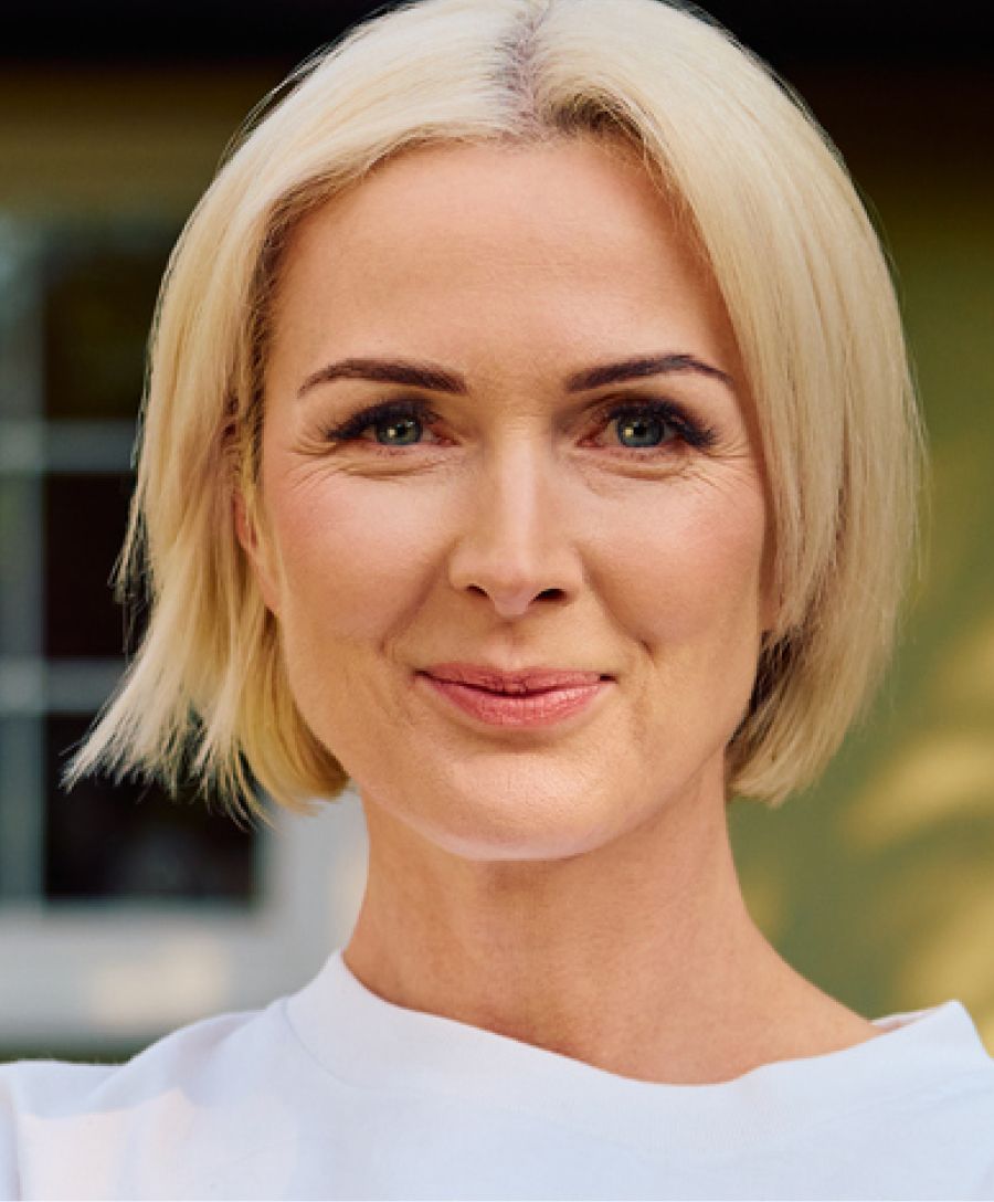 Smiling woman with short blonde hair outdoors.